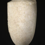 A cylinder-shaped marble vessel with a tapered top and a tapered base. The center of the vessel is engraved with the design of a seated man and a standing woman shaking hands. Side view.