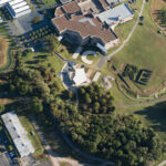 An aerial view of giant block letters that spell out “PICTURE THIS” on the ground. A building is on one side of the letters, and a grouping of trees is on the other.