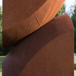 Detailed view of the area where the two rectangular shapes meet. Viewed from the side. The top section appears to be balancing on the bottom, but they are actually all one piece of metal.