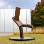 A geometric bronze sculpture on a lawn in front of a white building