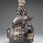 Side view of a ceramic sculpture depicting a bust with select painted faces below.