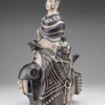 Angled view of a ceramic sculpture depicting a bust with select painted faces below.