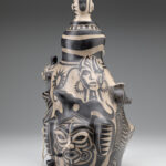Back view of a ceramic sculpture depicting a bust with select painted faces below.