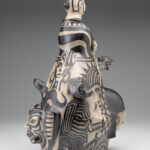 Angled view of a ceramic sculpture depicting a bust with select painted faces below.