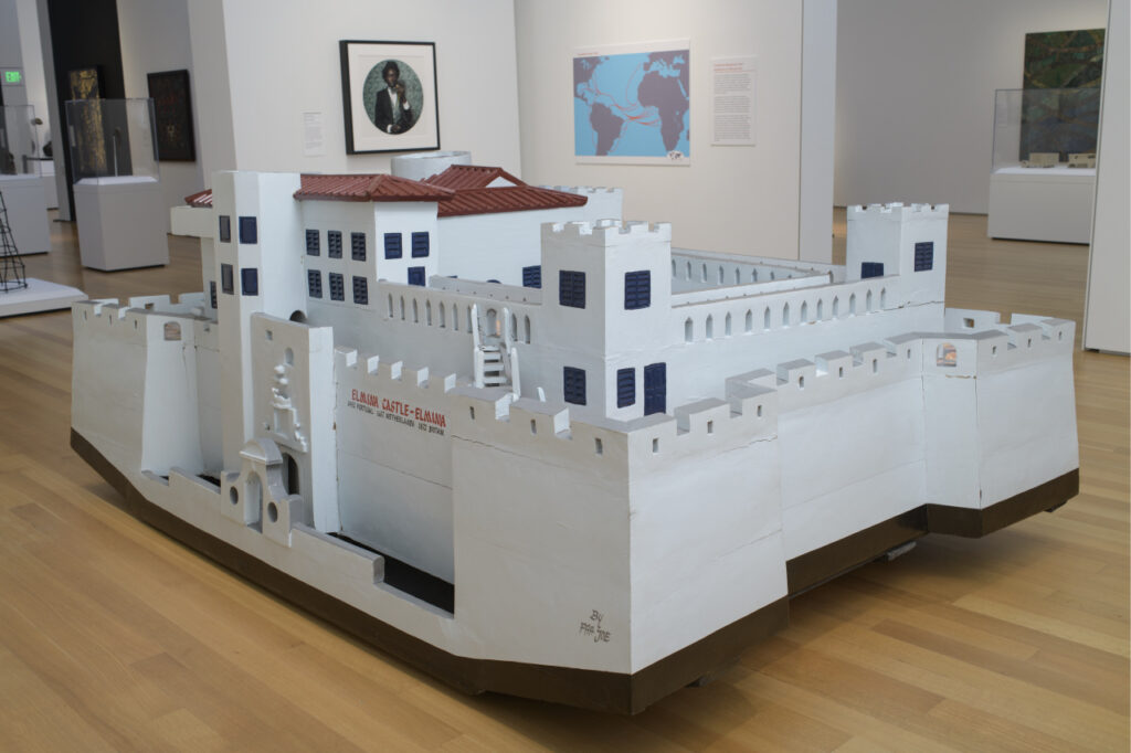 A large wooden sculpture of a white building with fortified towers and a reddish-brown roof