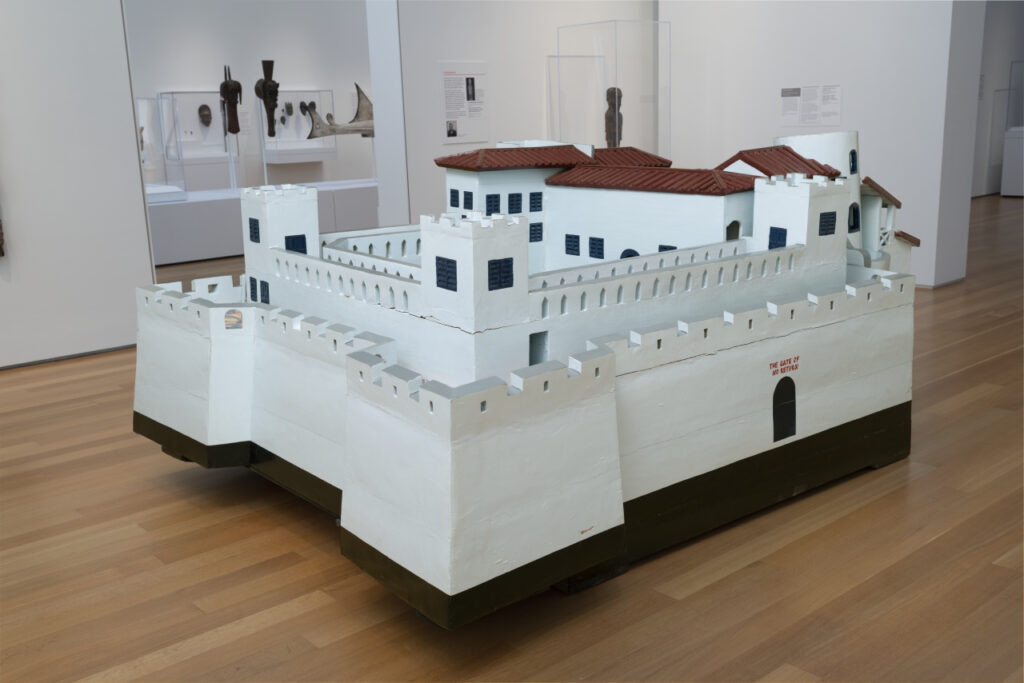 A large wooden sculpture of a white building with fortified towers and a reddish-brown roof