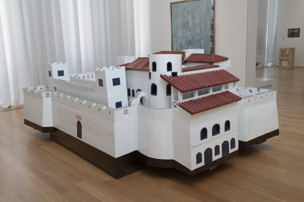 A large wooden sculpture of a white building with fortified towers and a reddish-brown roof