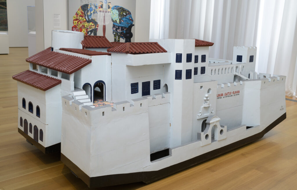 A large wooden sculpture of a white building with fortified towers and a reddish-brown roof