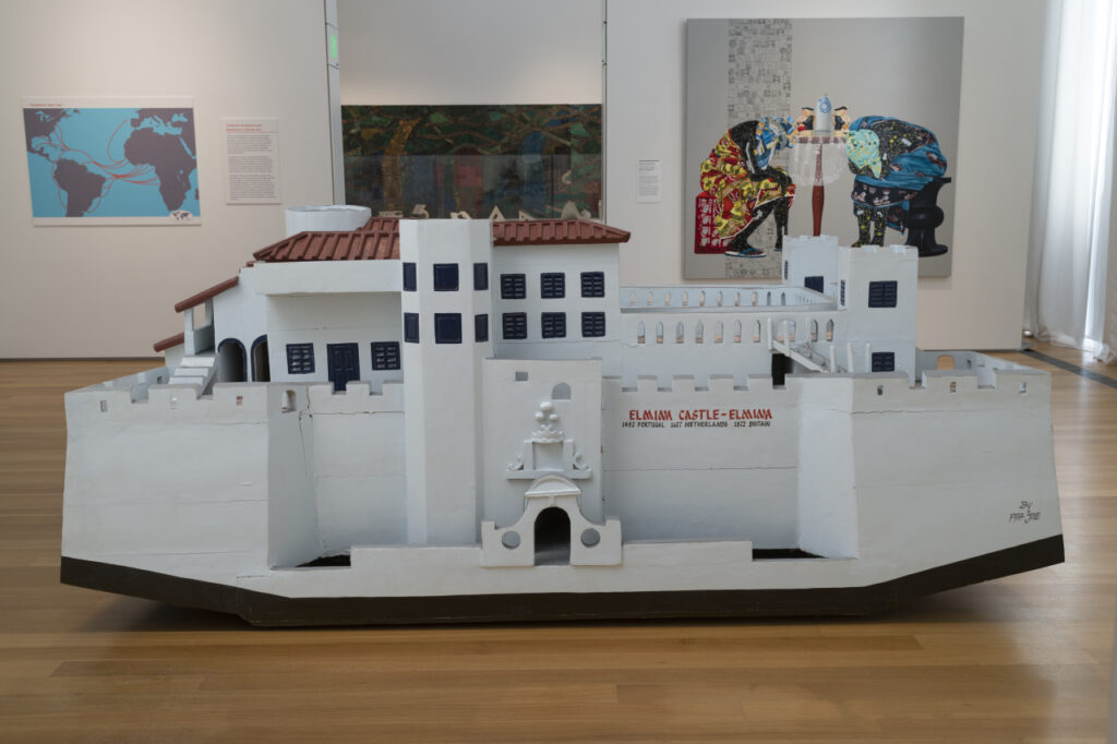 A large wooden sculpture of a white building with fortified towers and a reddish-brown roof