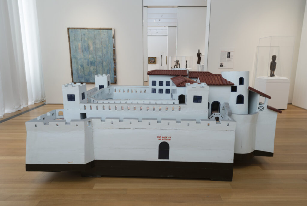 A large wooden sculpture of a white building with fortified towers and a reddish-brown roof