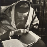 A black and white photo of a bearded man reading a Hebrew text