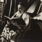 A black and white photo of a bearded man reading a Hebrew text