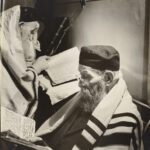 A black and white photo of bearded men reading Hebrew texts