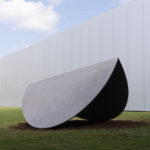 A large abstract sculpture of a folded elliptical shape in an outdoor setting