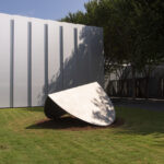 A large abstract sculpture of a folded elliptical shape in an outdoor setting