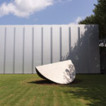 A large abstract sculpture of a folded elliptical shape in an outdoor setting