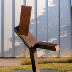 A geometric bronze sculpture on a lawn in front of a white building