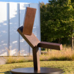 A geometric bronze sculpture on a lawn in front of a white building