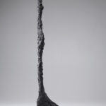 A bronze sculpture of an elongated nude female figure with oversized feet