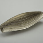 A silver cylindrical spice container with silver leafing on each tapered end