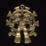 A round gold pendant with a two-headed figure sitting inside the inner circle