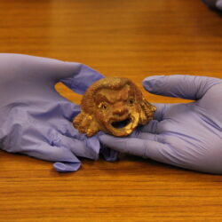 Gloved hands hold a terracotta sculpture of a face
