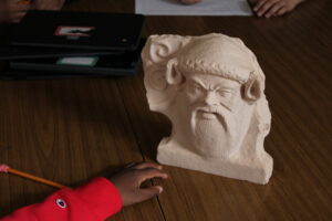 A child's hand reaches toward a 3D-printed replica of an ancient Greek antefix.