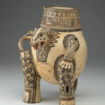 A painted terracotta vessel shaped like a crouching animal with patterned limbs and tail, open-mouth spout, and intricate black, cream, and red designs.