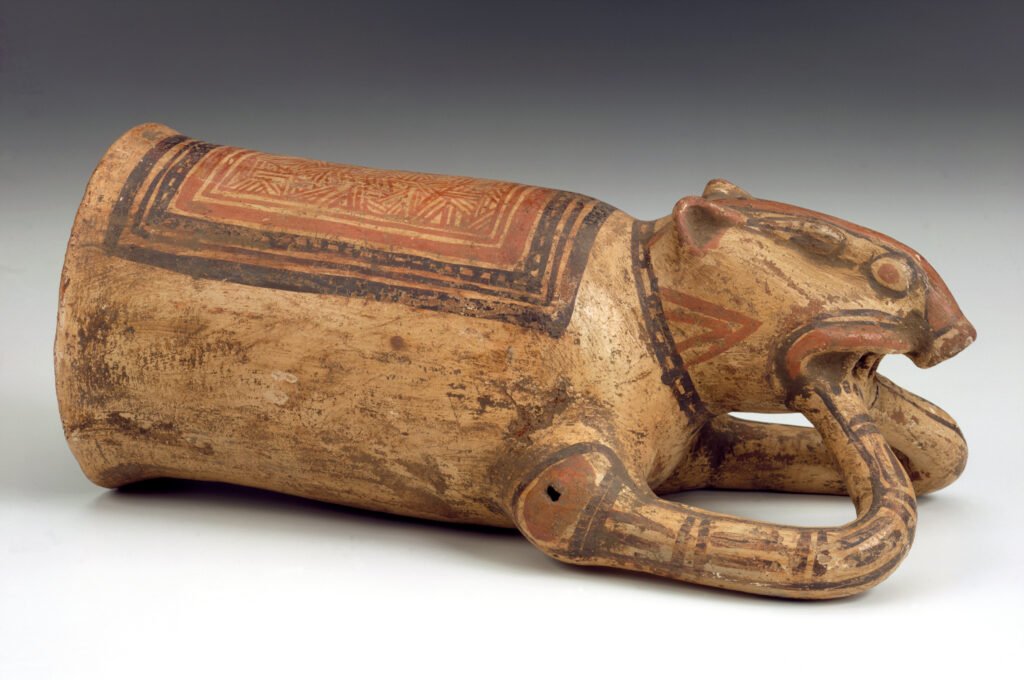 A ceramic drinking vessel positioned on its side, resembling a piglike animal decorated with red and black designs.