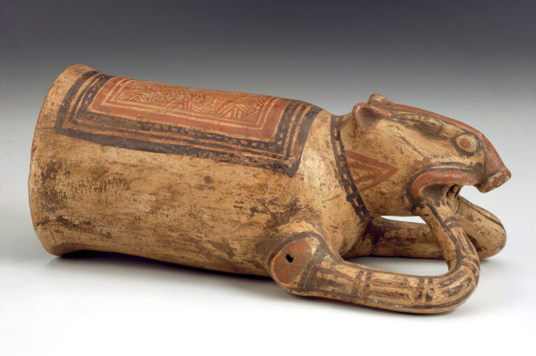 A ceramic drinking vessel positioned on its side, resembling a piglike animal decorated with red and black designs.