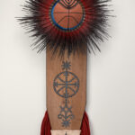 A mixed-media sculpture made of a wooden ironing board, cowrie shells, braided synthetic hair, shoe laces, clay pots, and a basketball.