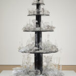 Sculpture made of five round wooden tiers painted black; each holds glass objects ranging from completely intact to broken and shattered.
