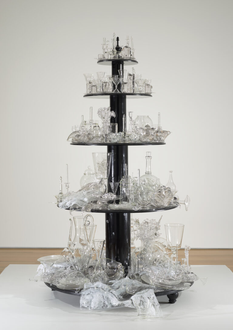 Sculpture made of five round wooden tiers painted black; each holds glass objects ranging from completely intact to broken and shattered.