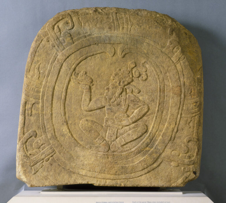 A tan, carved stone marker with a central design depicting a squatting man facing left.