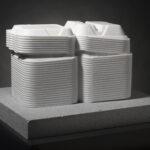 A white marble sculpture of open Styrofoam takeout boxes stacked on top of a gray, rectangle-shaped base.