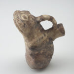Recipiente de cerámica con forma de rana, con un asa que conecta la parte superior de la cabeza de la rana con un pico en su espalda.