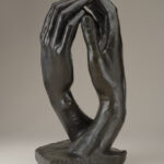 Bronze sculpture of two right hands facing each other with fingertips touching.