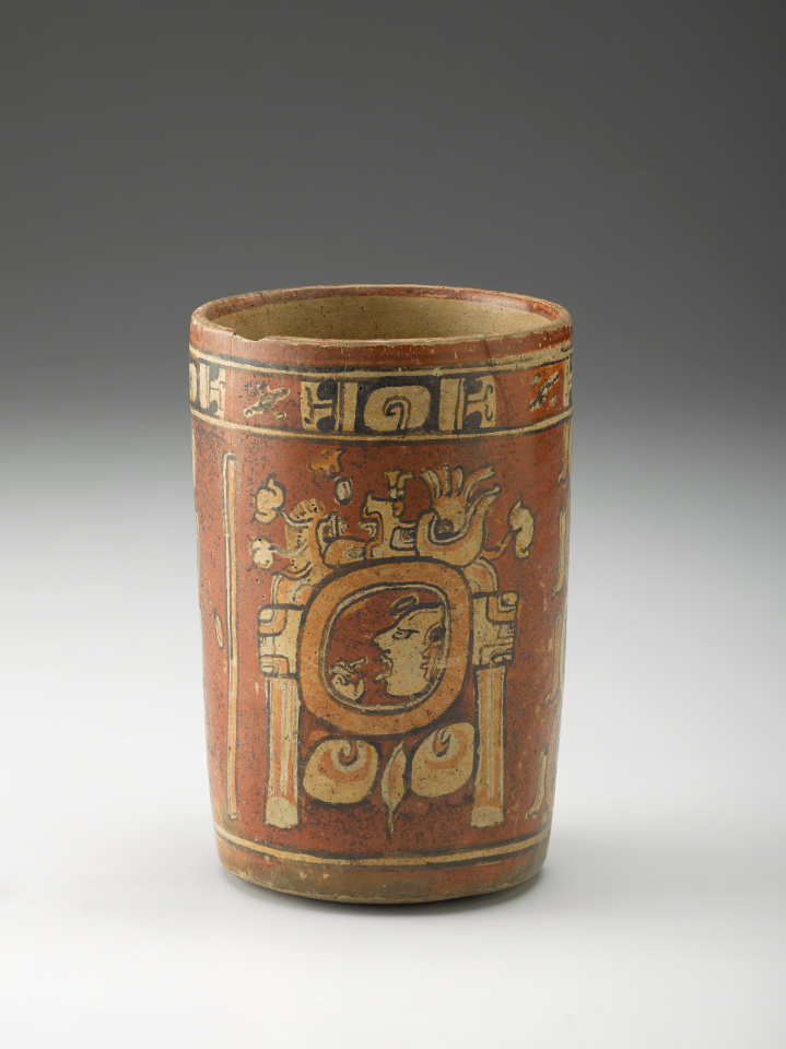 A red cylindrical ceramic vase decorated with designs and motifs in cream, black, and orange.