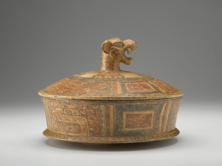 A terracotta cylindrical dish with a lid that has a jaguar-head handle. The dish is decorated with red and black designs.
